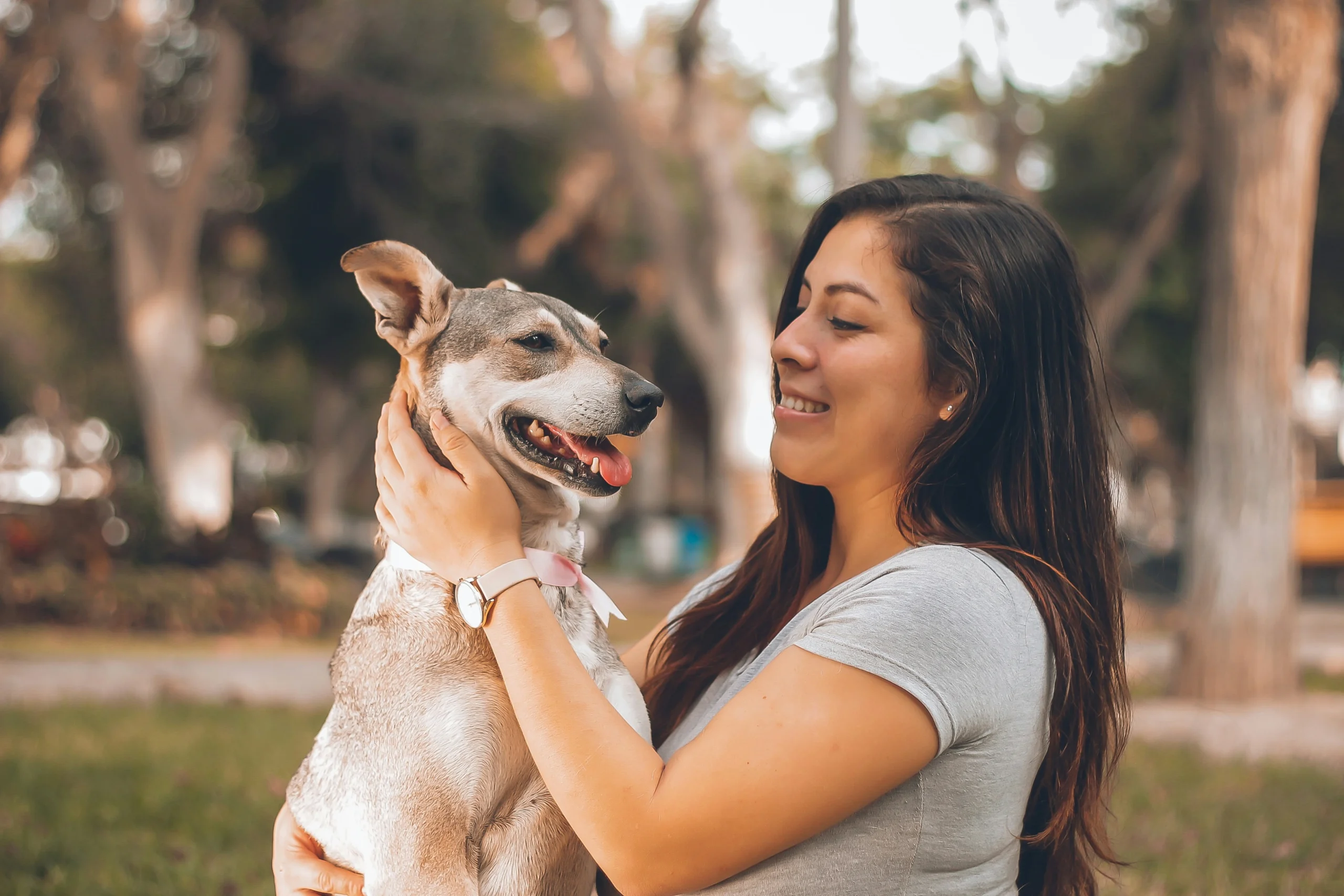 A woman holds her dog outdoors in a park.